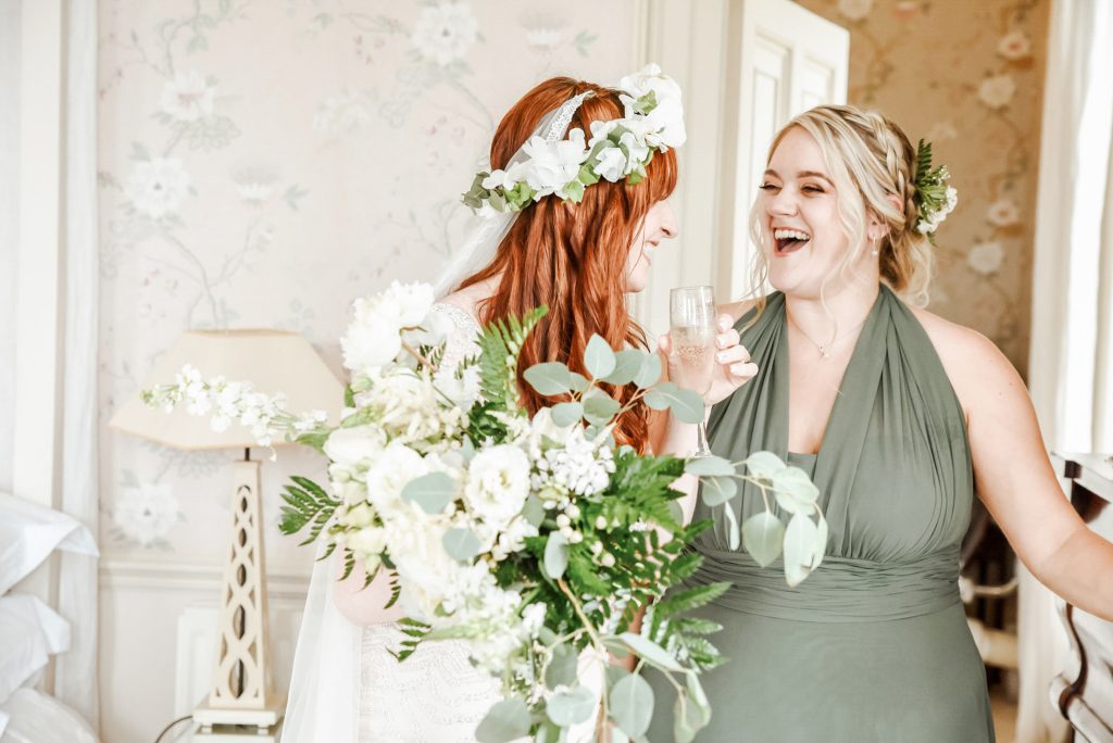 Bride celebrating with bridesmaids, drinking champagne and laughing before wedding at Drenagh Estate